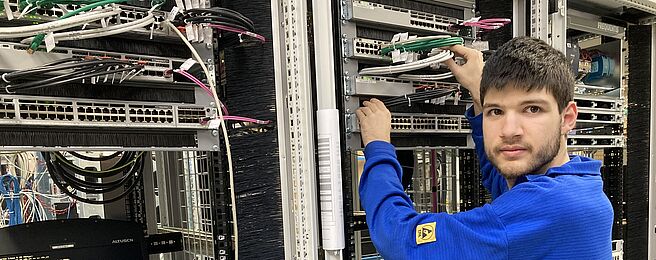 (c) Frequentis/Stradner Person in blauem Pullover arbeitet an einem Serverrack mit Netzwerkkabeln in einem Rechenzentrum.