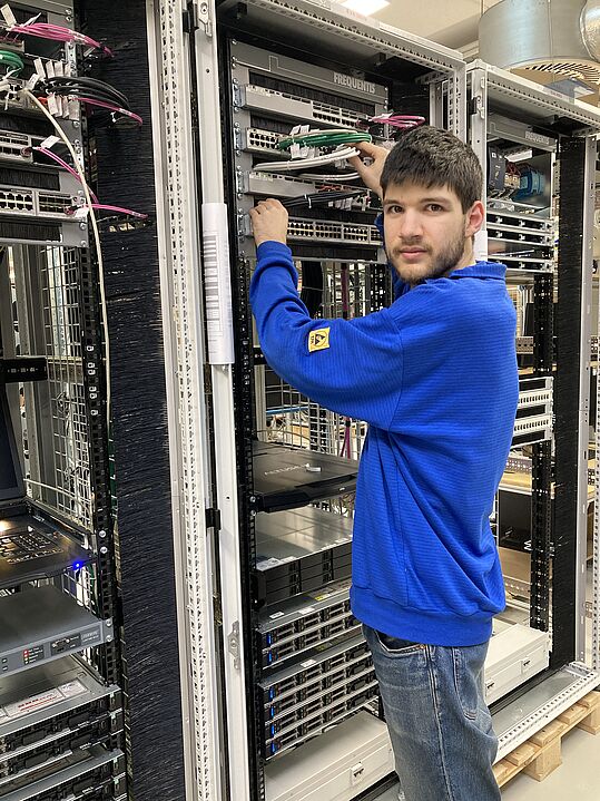(c) Frequentis/Stradner Person in blauem Pullover arbeitet an einem Serverrack mit Netzwerkkabeln in einem Rechenzentrum.