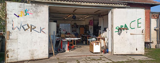 Offene Werkstatttore an einem Gebäude mit sichtbaren Werkzeugen und Werkbänken im Inneren