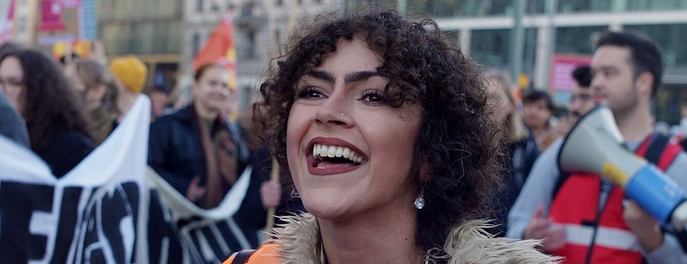 Das Bild zeigt eine lachende Person auf einer Demonstration.