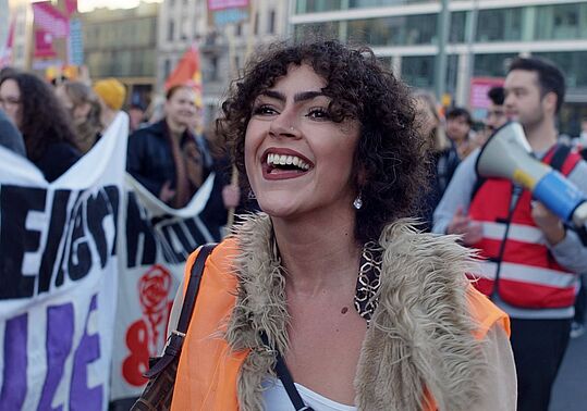 Das Bild zeigt eine lachende Person auf einer Demonstration.