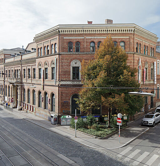 Eckgebäude aus rotem Backstein (WUK) mit mehreren Fenstern und Bäumen an der Straßenecke