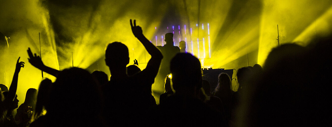 Europavox Vienna 2017 (c) Susanne Einzenberger Publikum vor einer Bühne mit gelber Bühnenbeleuchtung und DJ im Hintergrund