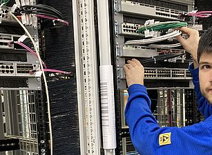 (c) Frequentis/Stradner Person in blauem Pullover arbeitet an einem Serverrack mit Netzwerkkabeln in einem Rechenzentrum.